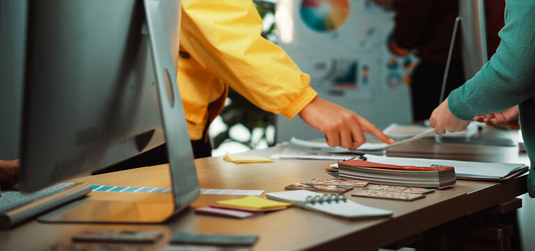 A collaborative workspace showcasing designers discussing and sharing ideas with technology and project materials on a modern office table, emphasizing creativity and teamwork. SACTR - Powered by Adobe