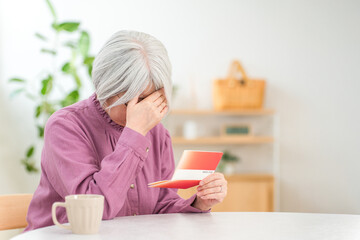 A worried, gray-haired senior woman is troubled by her savings passbook (financial troubles, bankruptcy in old age, personal bankruptcy)

