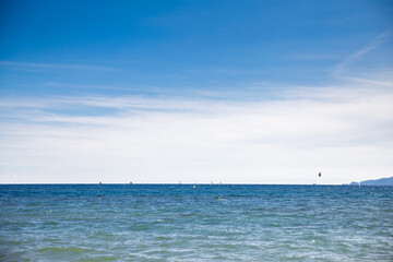 Minimal seascape on the French Riviera showing the Mediterranean horizon with small sailboats and a distant kitesurfer under a wide blue sky. Calm waves and open water provide tranquil mood.