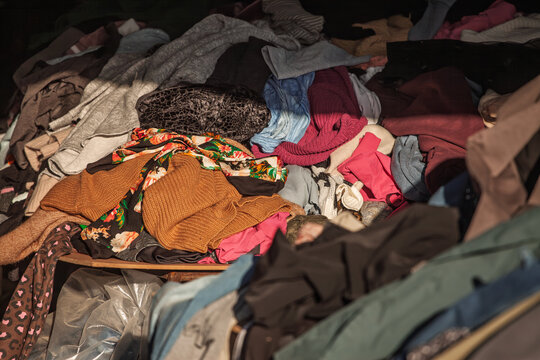 Piles of second hand clothes in a flea market, with mixed garments and colors in a casual heap. The scene evokes thrift shopping, resale, and the circular economy in everyday fashion.