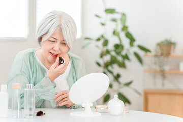 A senior Asian woman with gray hair applying makeup (lipstick, rouge, gloss, lip)
