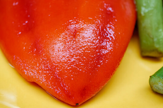 Extreme macro texture of the skin of a roasted red capia pepper showing the wrinkles and shiny oily surface details on a yellow plate