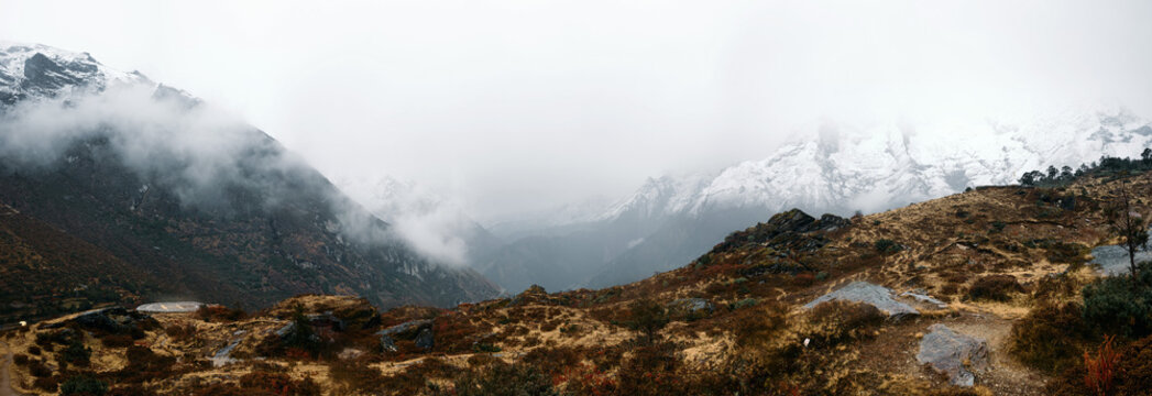 Cloudy mountain view with snow-capped peaks and mist over rocky terrain in the Himalayas during daytime - Powered by Adobe