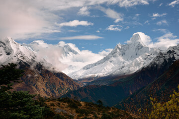 Fototapeta premium Mountains and clouds gather over snow-capped peaks during midday in a high-altitude landscape