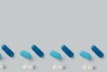 Arrangement of blue and white capsule pills on a light gray surface in a horizontal pattern