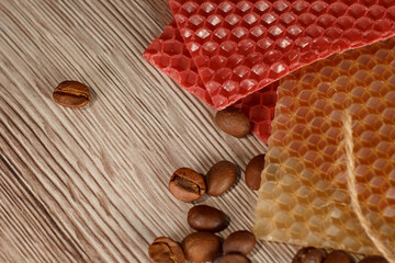 Close up of a beeswax candle with red honeycomb sheet and coffee beans on a wooden background