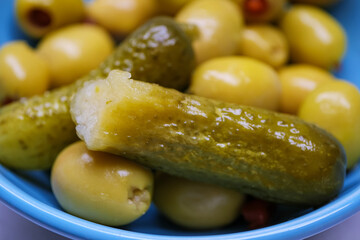 Macro detail of a bitten pickled cucumber resting on top of green olives showing the juicy interior and the crisp texture of the gherkin
