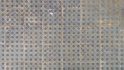 Close-up of gray tactile paving slabs with raised dot pattern for visually impaired assistance. Hydraulic cement tiles, square pedestrian tile floor texture. Accessibility, urban environment, outdoor
