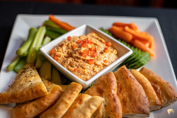 Roasted red pepper hummus served with pita bread cucumbers carrots at a high end wine bar and restaurant