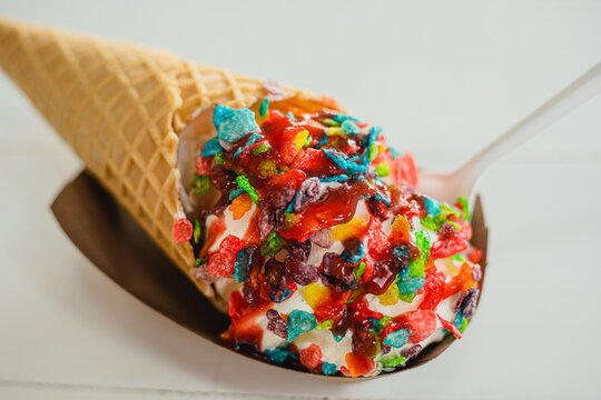 A vanilla ice cream cone topped with colorful fruity pebbles cereal