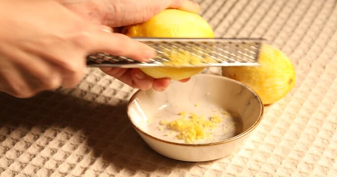 Woman zesting lemon with grater at table, closeup