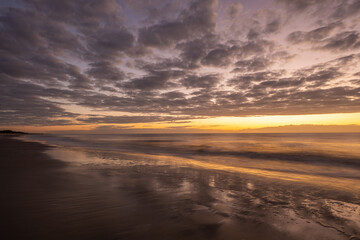 Obraz premium Sunrise at the beach with cloudy sky and smooth sand during morning hours