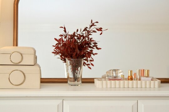Dresser with ceramic perfume tray, jewelry boxes, and vase with maroon leaves