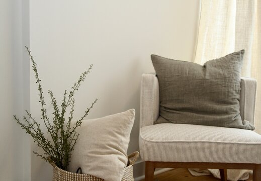 Modern greige armchair with linen grey pillow with woven basket filled with pillow and green branches