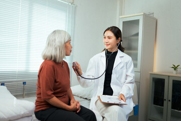 Obraz premium Female doctor checking elderly patient's heartbeat with stethoscope