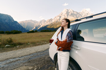 Obraz premium woman car mountains road travel nature landscape portrait. Young woman leans on white SUV at roadside, enjoying a scenic mountain view during a road trip, outdoor adventure and freedom.
