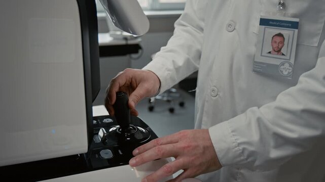 Tilt up shot of doctor operating control joystick on modern ophthalmic diagnostic device during eye examination in clinic, focus flowing from hands to face, copy space