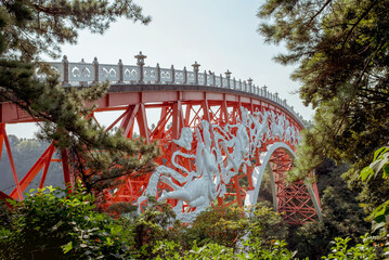 A striking red bridge with intricate sculptures in a lush setting on Jeju Island, Korea, blending art and nature seamlessly