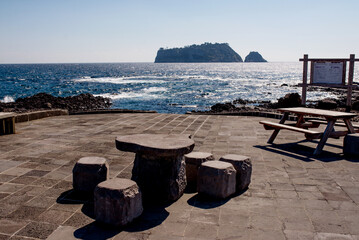 Serene rest area on Jeju Island with stone seating and panoramic ocean views, perfect for relaxation