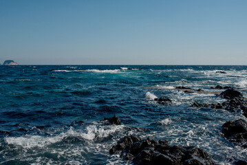 Dynamic ocean waves rolling onto the rugged rocks of Jeju Island, showcasing the islands natural beauty and coastal charm