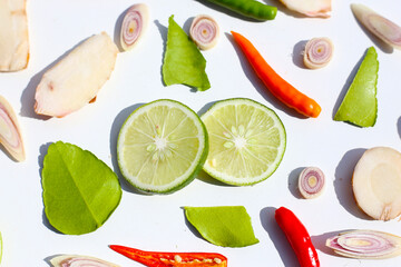A colorful, close-up pattern of Thai herbs: lime slices, galangal, lemongrass, chilies, and kaffir lime leaves.