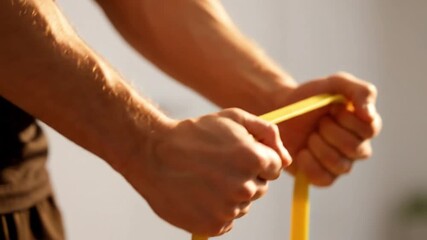 A male athlete's strong hands gripping and pulling a yellow rubber resistance loop for a powerful arm and shoulder workout or physical therapy