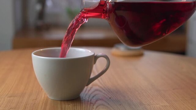 mesmerizing slowmotion pour of vibrant red herbal tea from an elegant glass teapot into a ceramic cup, highlighting cozy teatime atmosphere