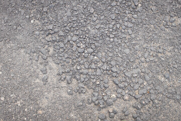 A close-up of weathered asphalt with visible embedded stones and gravel, showing rough texture and signs of erosion.