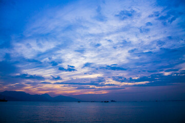 Obraz premium A tranquil coastal scene at dusk with boats, mountains, and a sky filled with blue, purple, and orange hues.
