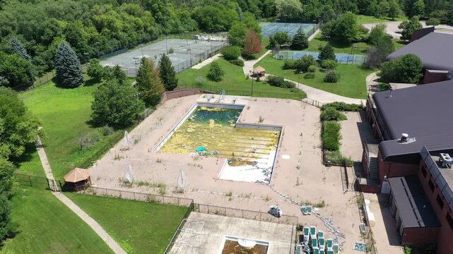Aerial view of an abandoned sports club with crumbling tennis and pickleball courts and filthy swimming pool.