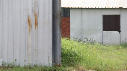 Dilapidated white metal building sits on overgrown lot in rural area, showing signs of neglect and decay, evoking a sense of abandonment and decay.