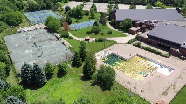 Aerial view of an abandoned sports club with crumbling tennis and pickleball courts and filthy swimming pool.