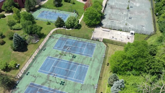 Aerial view of an abandoned sports club with crumbling tennis and pickleball courts and filthy swimming pool.