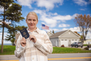 Smiling woman holding a United States passport outdoors with an American flag and suburban homes behind her