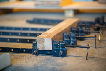 Set of clamps tools instruments for compressing and gluing wooden beams laying on work table in carpentry workshop, small business woodshop creating handmade items and furniture for home and living.