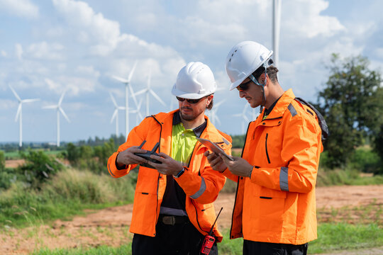Renewable energy engineers review wind farm project plans and data to analyze the efficiency and safety of wind power generation systems. - Powered by Adobe