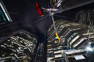 Fototapeta premium Night reflections rise into a maze of glass and steel as a glowing traffic light hangs beneath towering skyscrapers. The scene feels like a futuristic canyon where geometry, light