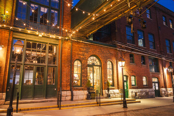 Fototapeta premium Historic brick architecture illuminated by warm streetlights and string lights in the Distillery District of Toronto at night.