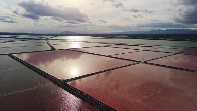 Aerial drone view of colorful salt ponds near Santa Pola, Spain, with pink and green water reflecting clouds and sunlight over the Mediterranean coast.