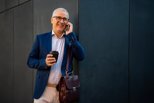 Mature businessman smiling talking on smartphone drinking coffee