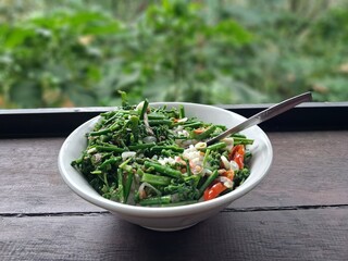 A bowl of stir-fried ferns on a table with a view of the green forest.