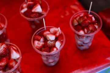 Delicious strawberry dessert in plastic cup with cream, sweet tasty snack. This fresh food treat on red background, refreshing sweet, popular street food