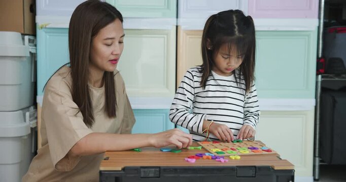  Mother and her young daughter are engaged in an educational activity at home, placing colorful letter and number pieces into a wooden puzzle board 