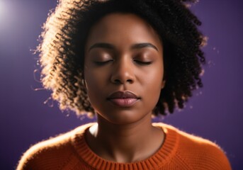 Serene african american woman meditating with closed eyes illuminated by warm light on purple