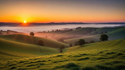 Obraz premium Sunrise over rolling green hills with morning mist and golden light.