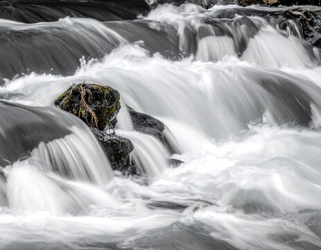 Flowing water cascades down rocks in a grayscale photograph - Powered by Adobe