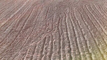 Slow Aerial Pan Over Dry Brown Soil With Irregular Patterns And Stones Showing The Raw Texture Of Arable Land Before Cultivation