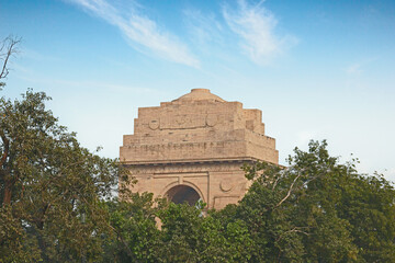 Delhi, India, November 28, 2025: Scenic wide view of the historic India Gate monument surrounded by green trees and manicured gardens at Kartavya Path under a blue sky.