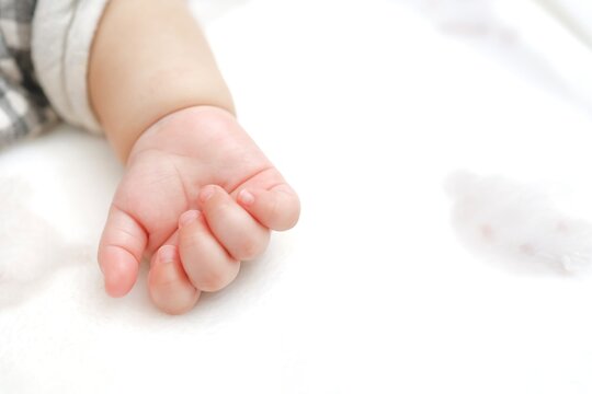 白い布団に添えられた赤ちゃんの小さな手のアップ。