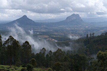 Panoramic View of Lush Green Landscape with Mist and Two Prominent Mountain Peaks Under Cloudy Sky